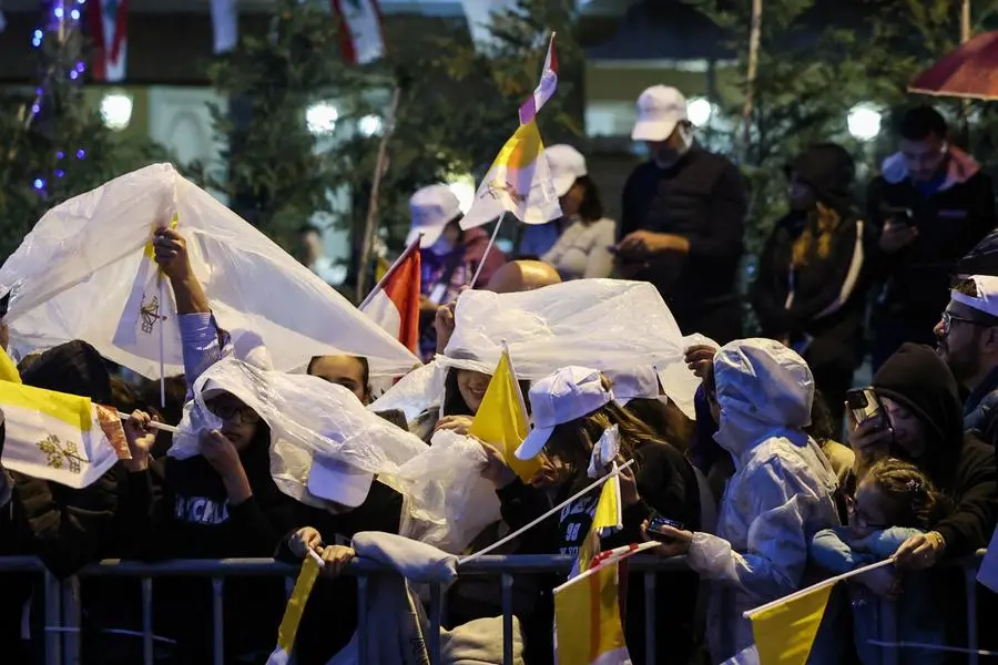 I fedeli libanesi sotto la pioggia con le bandierine del Vaticano attendono il passaggio del Papa