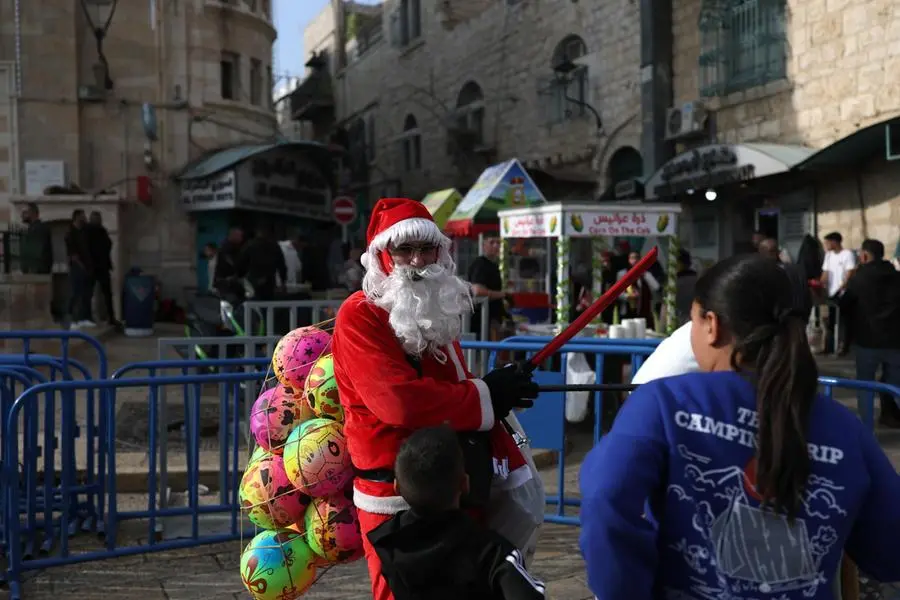 epa12574252 A man dressed as Santa Claus stands in Manger Square ahead of the lighting of the Christmas tree, in the West Bank city of Bethlehem, 06 December 2025. Bethlehem's Christmas tree in Manger Square, adjacent to the Church of the Nativity, is scheduled to be lit on 06 December, marking the city's first celebration in two years. EPA/ATEF SAFADI