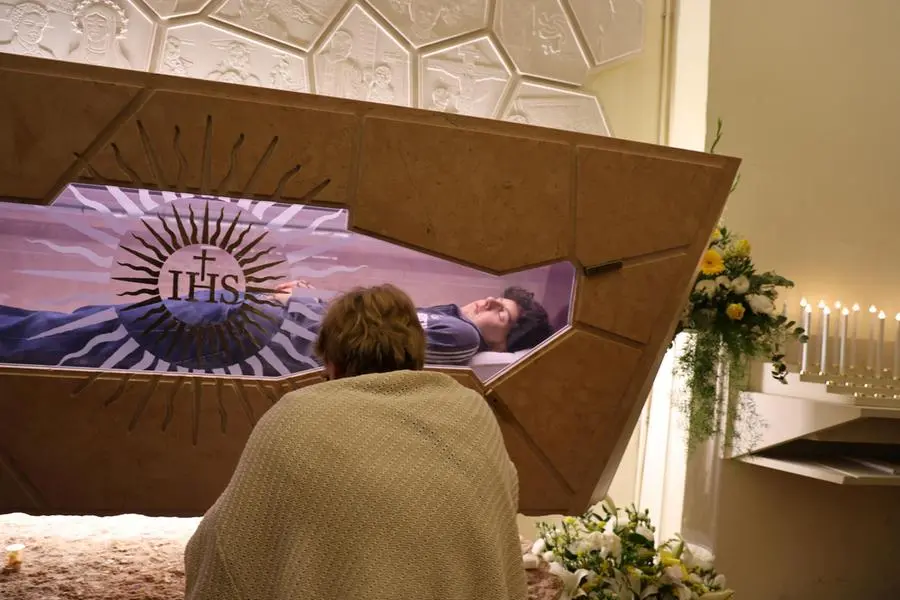 Una donna in preghiera davanti alle spoglie mortali di San Carlo Acutis custodite nel Santuario della Spogliazione di Assisi