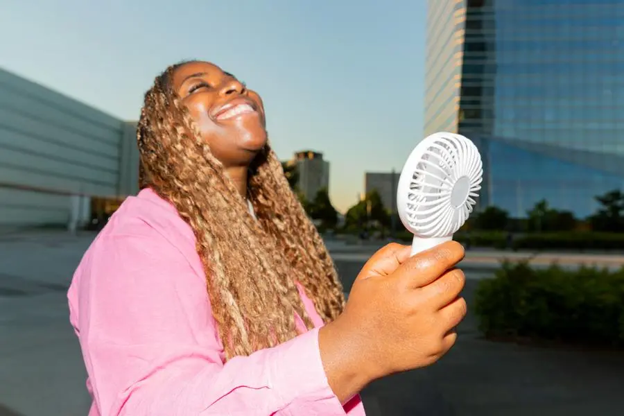 Smiling woman enjoying refreshing breeze from portable fan in urban setting