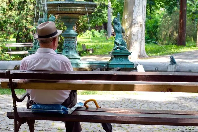A lonely old man sitting on a bench in a park, looking at fountain , Getty Images