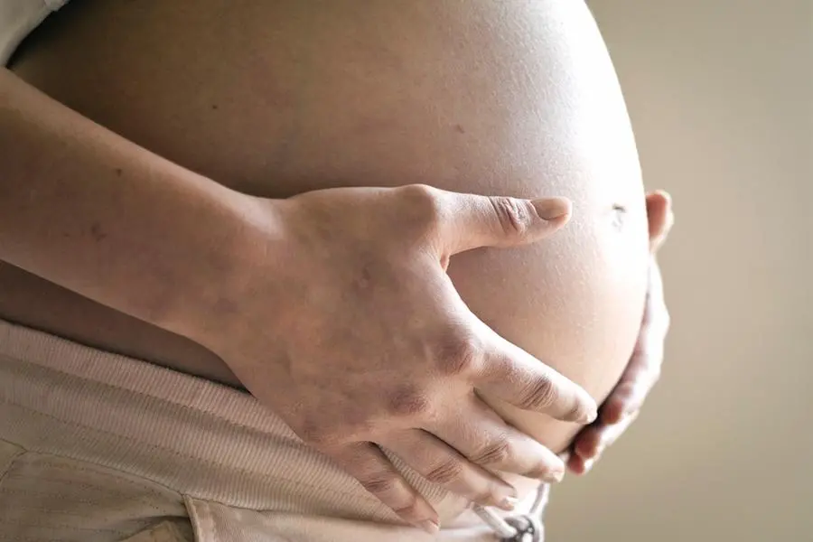 Pregnant woman supporting her pregnant abdomen with her hands. , Getty Images