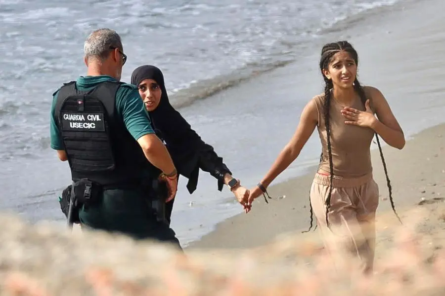 Un agente della Guardia Civil parla con due donne sulla spiaggia mentre i migranti raggiungono il territorio spagnolo dopo essere arrivati a nuoto dal Marocco a Ceuta, un\\'enclave spagnola nel Nord Africa , EPA