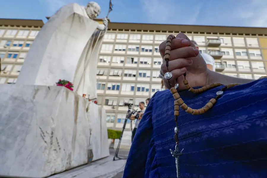 Fedeli in preghiera davanti alla statua di san Giovanni Paolo II all’esterno del Policlinico Gemelli di Roma, dove è ricoverato papa Leone XIV