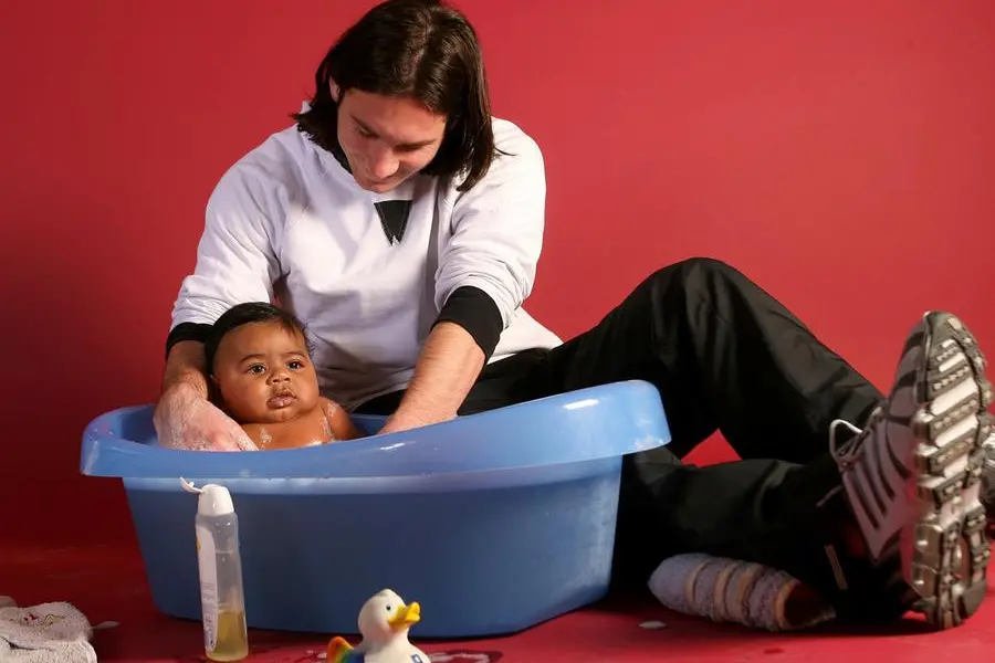 Un giovanissimo Messi fotografato mentre fa il bagnetto a Yamal neonato, nello scatto per il calendario Unicef. Foto di Joan Monfort , AP