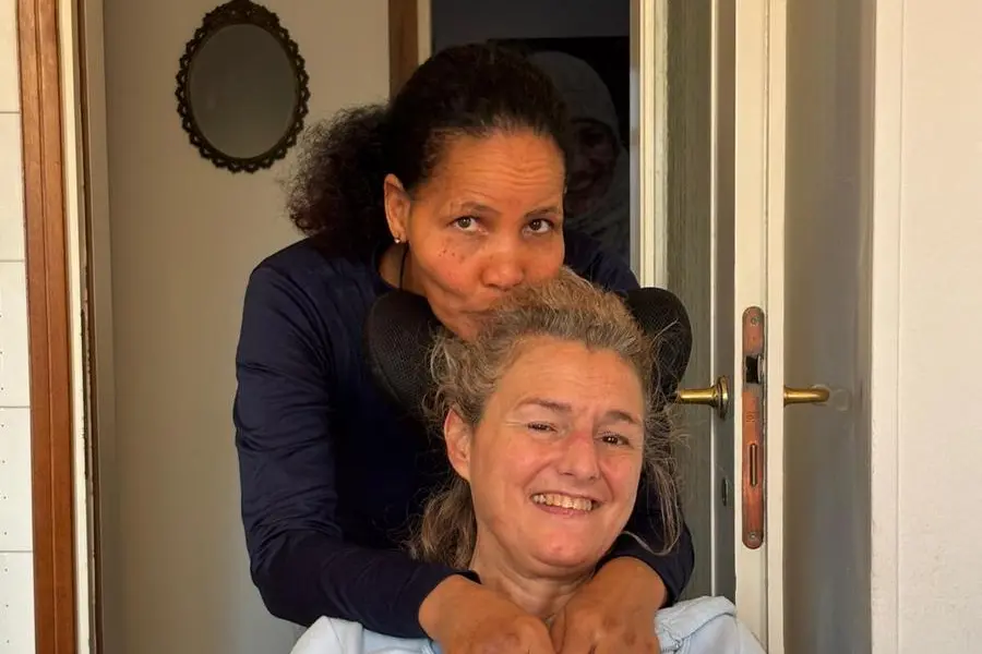 Un momento della quotidianit\\u00E0 di Mary Sangalli, 54 anni, insieme a Yordanos, che la assiste da qualche anno. A fianco: Il libro, Ci\\u00F2 che mi sorprende. La vita scritta con gli occhi (Edizioni Ares), che Mary ha dedicato ai figli.