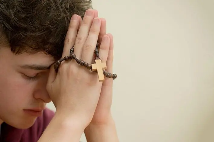 Teenage boy praying with a rosary , Ben Gingell - stock.adobe.com