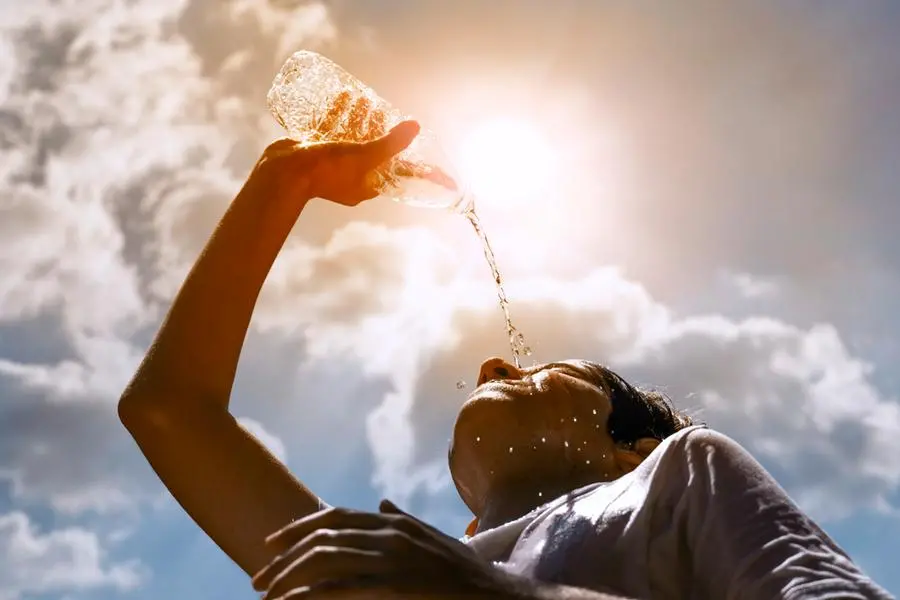 Young woman drinking fresh water from a plastic bottle under the hot summer sun , Getty Images