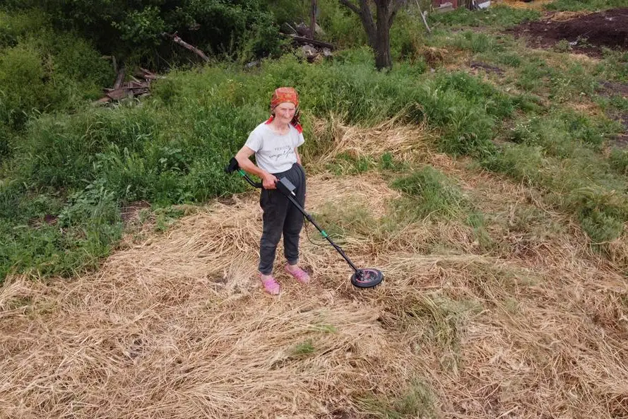 A woman in the Mykolaiv region uses a metal detector to find landmines in a plot near her house.