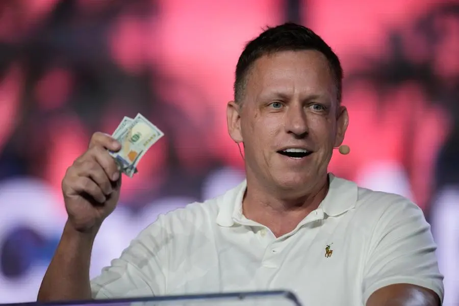 FILE - Peter Thiel, co-founder of PayPal and Palantir, offers a pair of hundred dollar bills to attendees during a keynote address at the Bitcoin Conference, April 7, 2022, in Miami Beach, Fla. , (AP Photo/Rebecca Blackwell, File)