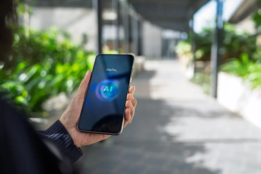 Close-up of a person holding a smartphone displaying an AI assistant interface outdoors, illustrating multimodal artificial intelligence technology that combines text, voice, and visual interaction for intelligent communication and support in everyday environments.