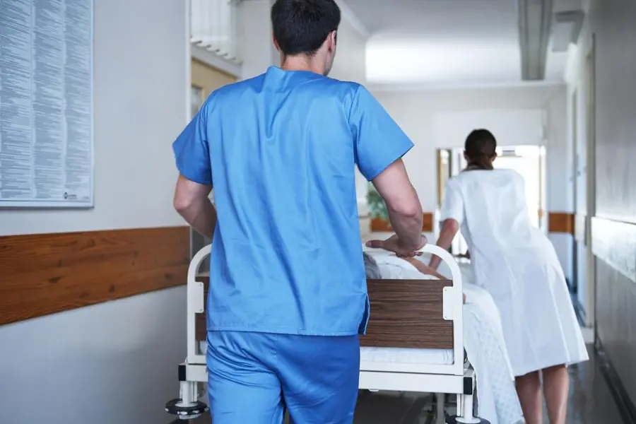 Rearview shot of hospital staff wheeling a patient in a gurney down a corridor , Getty Images