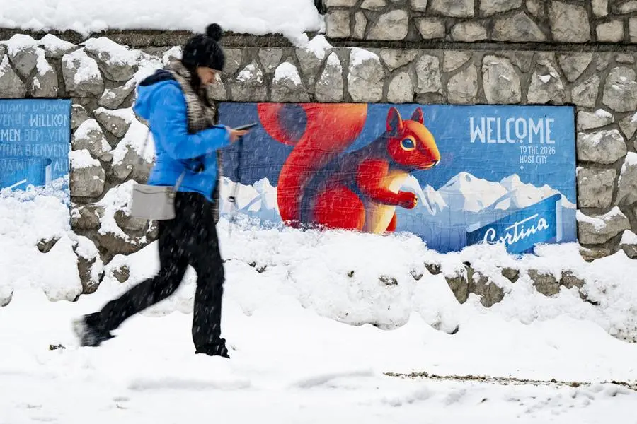 Una donna a Cortina d\\'Ampezzo passa davanti a uno striscione con la scritta \\u201CBenvenuti nella citt\\u00E0 ospitante del 2026\\u201D in vista dei Giochi Olimpici Invernali Milano Cortina 2026 , EPA