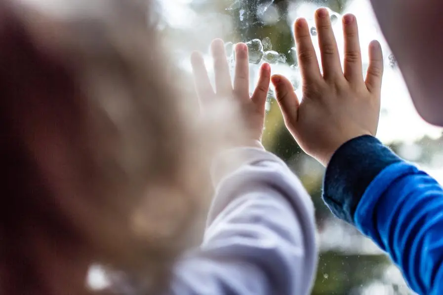 Close-up of hands of a boy and a girl. They are touching the window and watching first snow. , iStock
