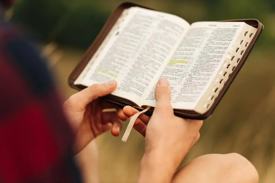 Reading the Bible outdoors in nature. A man in sunglasses and a shlap holds a Bible in his hands, standing in the forest. Faith, spirituality and religion concept , Shopping King Louie - stock.adob