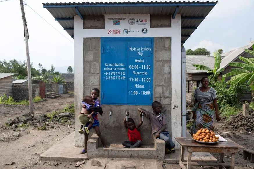 In questa immagine del giugno 2025 si vedono alcuni bambini mentre giocano davanti a un chiosco di acqua potabile fuori servizio, che avrebbe dovuto essere alimentato dal serbatoio idrico. Collegamenti idrici incompleti, dovuti ai tagli ai fondi USAID destinati all\\u2019ONG Mercy Corps, hanno causato continue carenze d\\u2019acqua a Goma, nella provincia del Nord Kivu, nella Repubblica Democratica del Congo , REUTERS