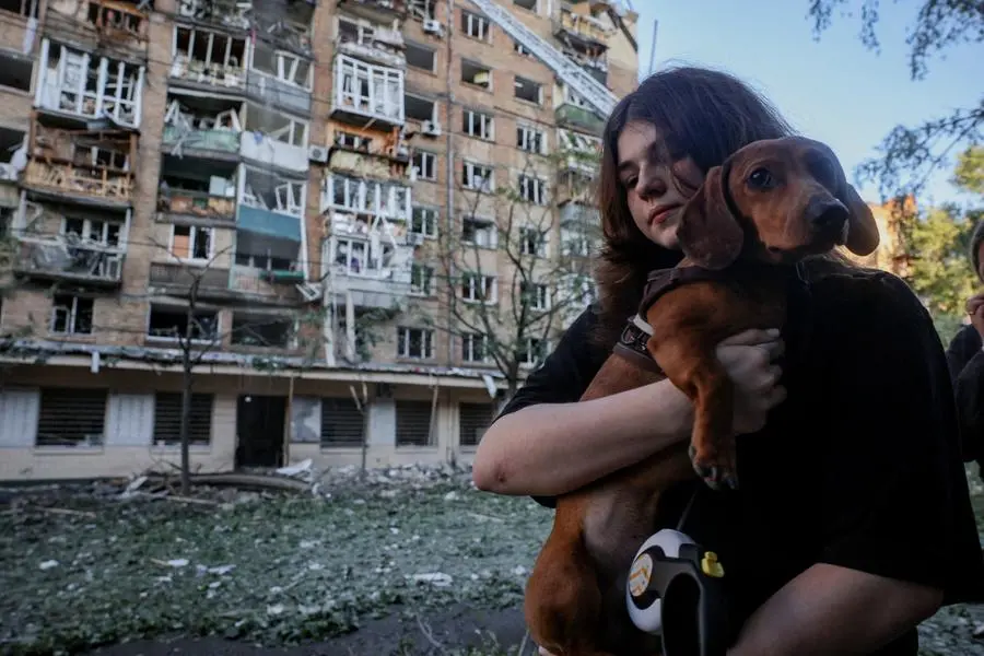 Una ragazzina con il suo cane passa davanti a un edificio colpito dall'attacco russo su Kyiv.