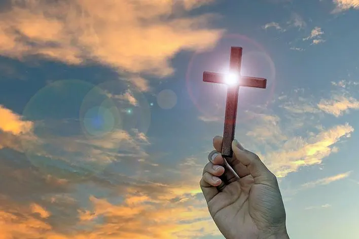Silhouette hand holding wood cross against sunrise background, open palm up worship, pray for blessings from God. Christian Religion, Crucifix and Faith concept , Jo Panuwat D - stock.adobe.com