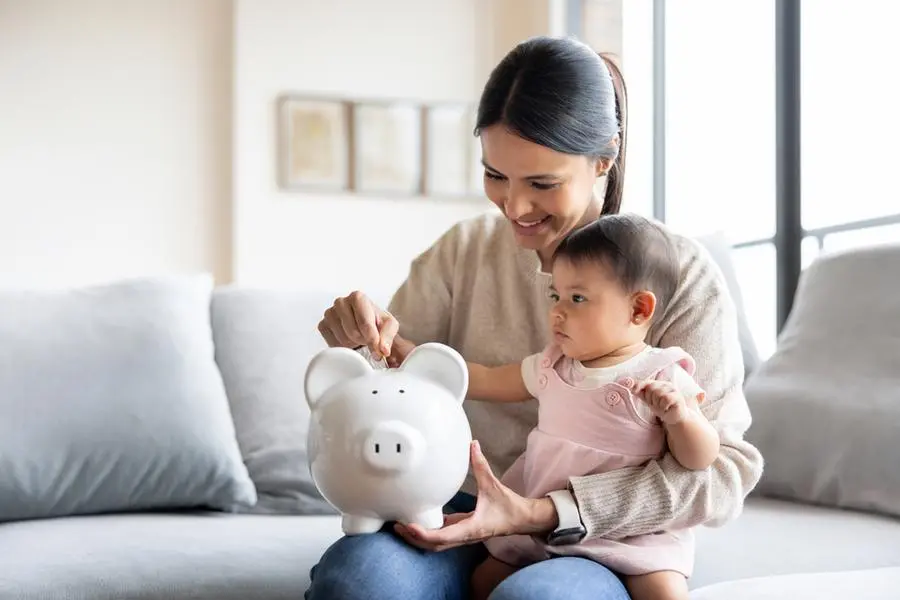 Happy Latin American mother saving money for her baby\\'s future in a piggy bank - family concepts , Getty Images