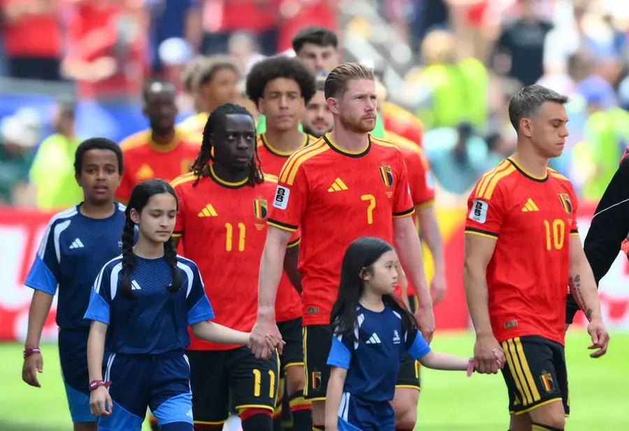 Jeremy Doku enters the field holding the hand of a child.