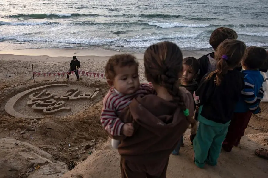 Alcuni bambini palestinesi osservano una scultura di sabbia con la scritta “Benvenuto, Ramadan”, realizzata dall'artista palestinese Yazeed Abu Jarad, su una spiaggia di Khan Yunis, nella Striscia di Gaza meridionale