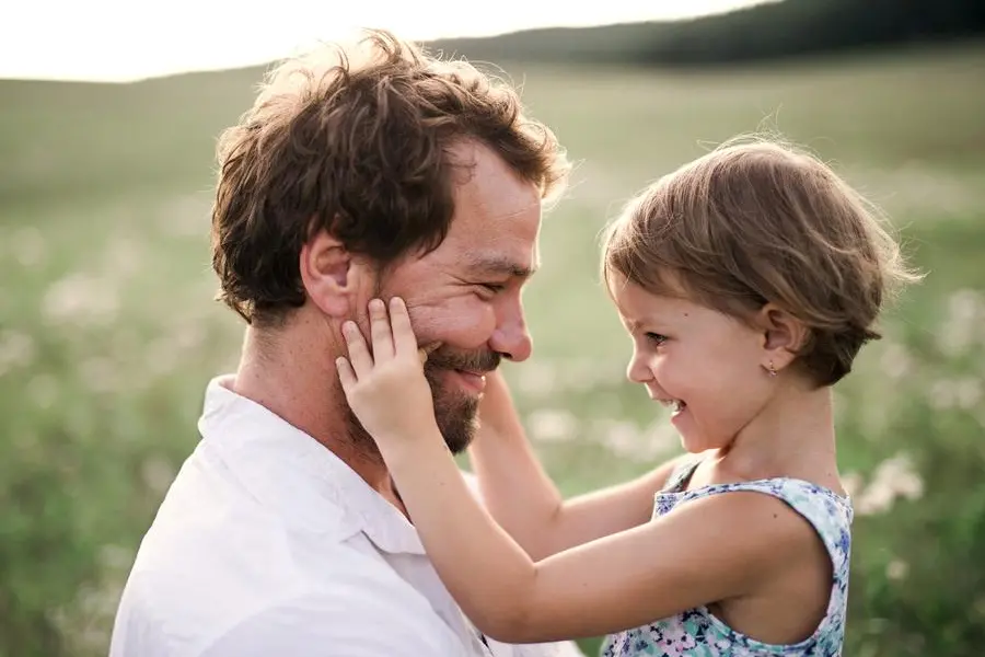 Handsome young father in green sunny summer nature holding his cute small daughter in the arms.