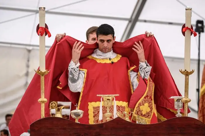 A priest is helped to get dressed before giving Communion during an ordination ceremony of the traditionalist Catholic Society of Saint Pius X (SSPX), in Econe, near Sion, western Switzerland, on June 29, 2026. Defying Vatican, Society of Saint Pius X will ordain its own bishops on July 1, 2026, despite the risk of being considered schismatic. (Photo by Fabrice COFFRINI / AFP)
